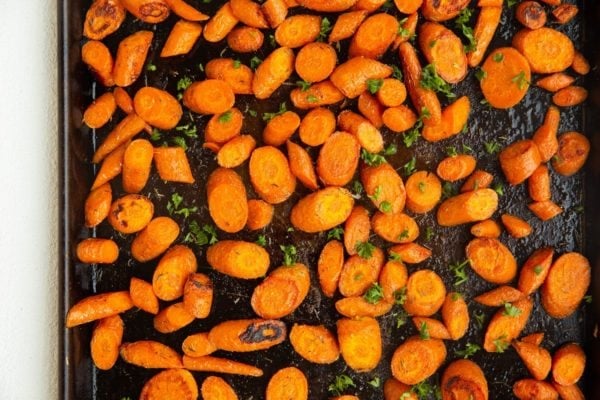 Roasted carrots fresh out of the oven on a baking sheet sprinkled with fresh parsley