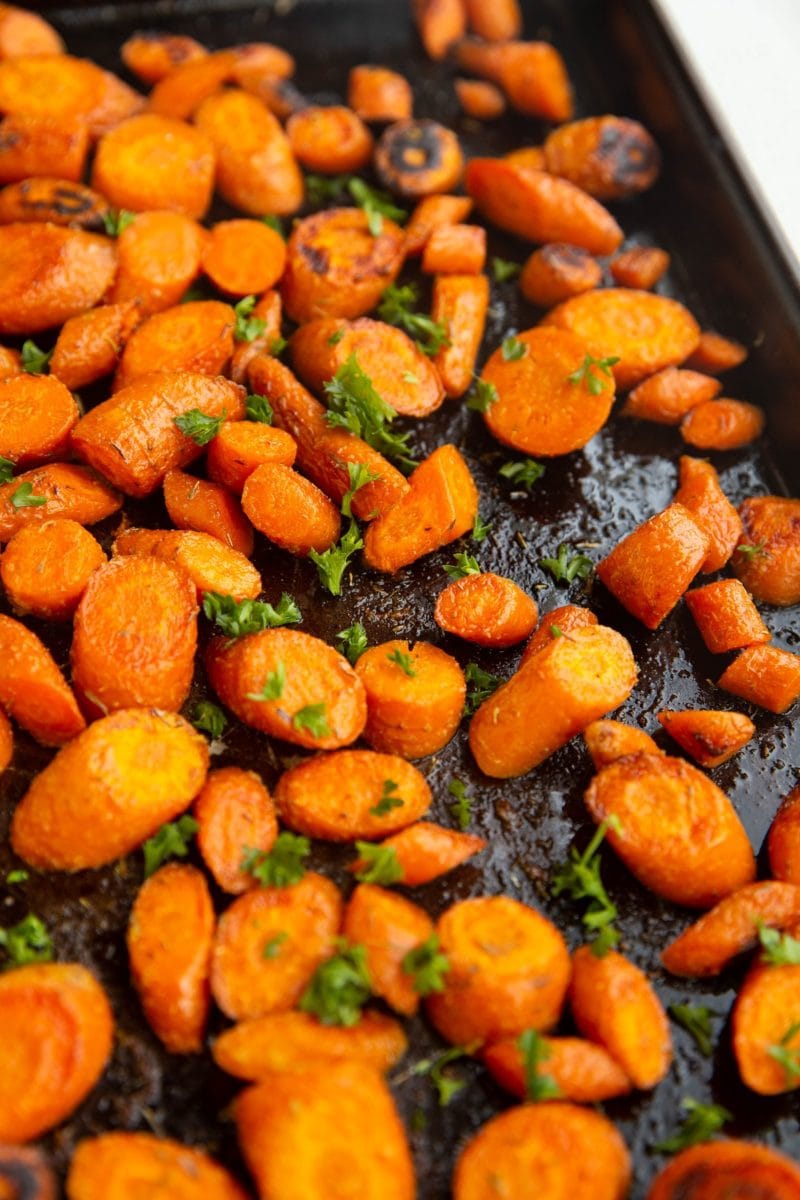 Roasted carrots spread over a large baking sheet, sprinkled with fresh parsley.