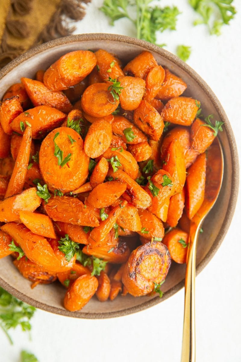 Roasted carrots in a bowl with a golden spoon, ready to serve.