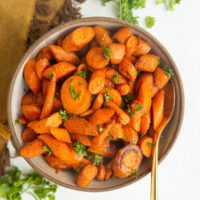 Roasted carrots in a bowl with a golden spoon, ready to serve. Fresh parsley to the side along with a golden napkin.