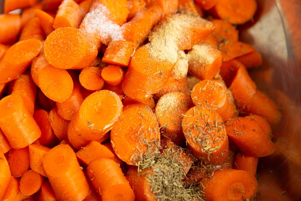 raw carrots in a mixing bowl with oil, salt and spices