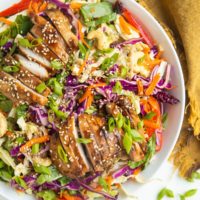 Big bowl of Asian sesame ginger chopped salad with sliced chicken on top and a golden napkin to the side.