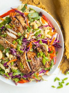 Big bowl of Asian sesame ginger chopped salad with sliced chicken on top and a golden napkin to the side.