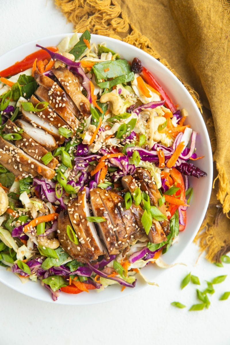 Big bowl of Asian sesame ginger chopped salad with sliced chicken on top and a golden napkin to the side.