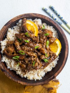 Big wooden bowl of brown rice and sesame ginger orange beef with chopsticks to the side.