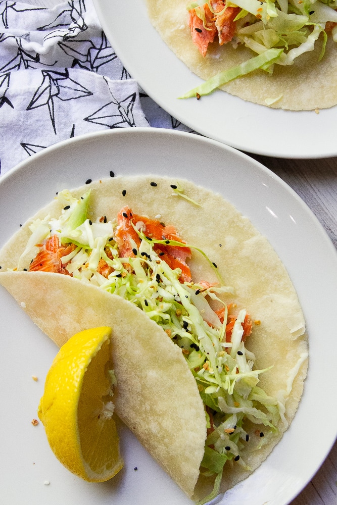 Smoked salmon tacos on white plates with a lemon wedge.