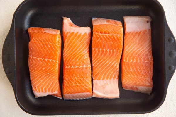 four raw salmon filets in a casserole dish