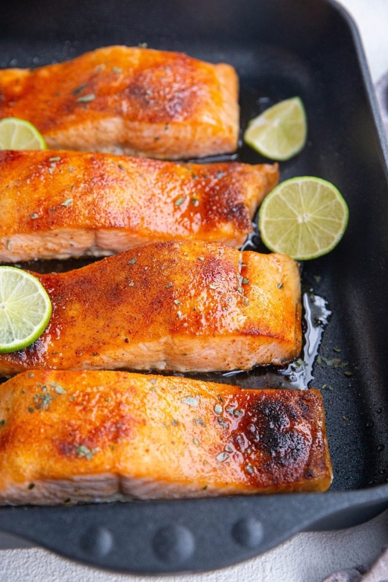 Oven Roasted Glazed Salmon in a black casserole dish with lime slices on top.