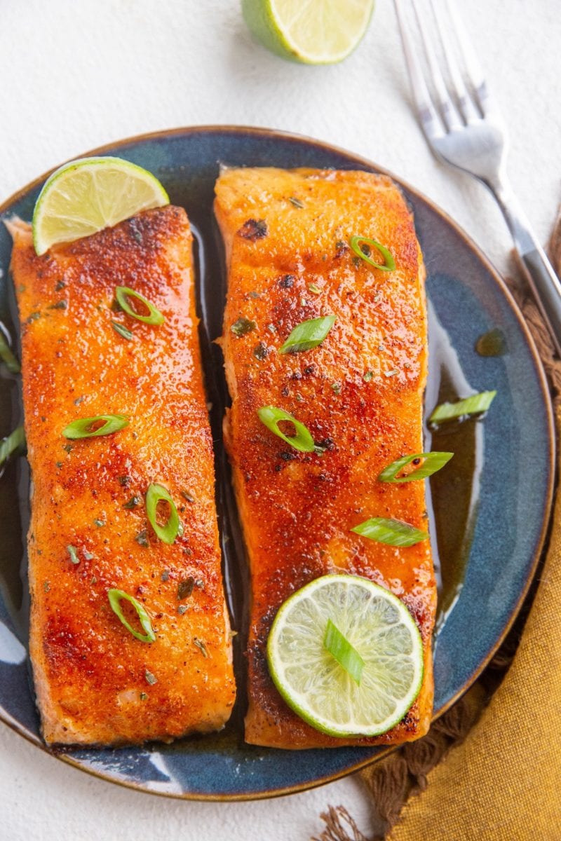Two glazed salmon fillets on a blue plate with a fork to the side and lime slices.