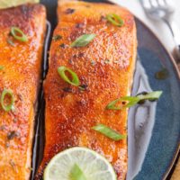 Two cooked salmon filets on a plate with green onion on top.