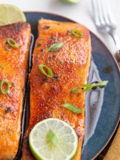 Two cooked salmon filets on a plate with green onion on top.