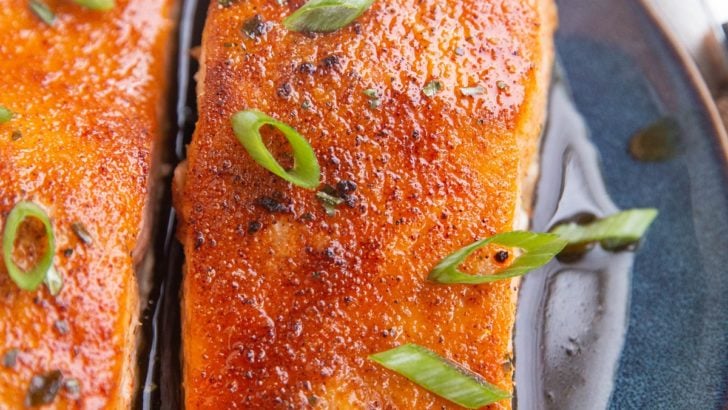 Two cooked salmon filets on a plate with green onion on top.