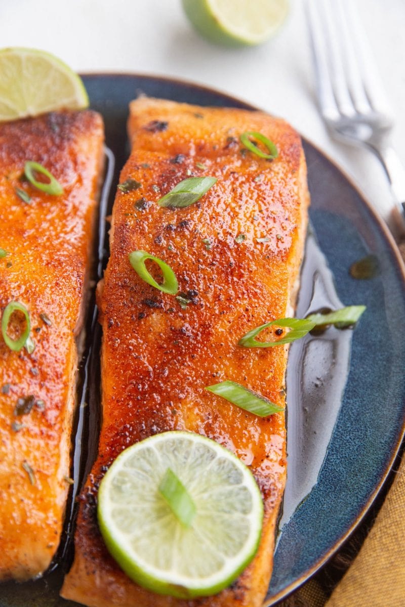 Two cooked salmon filets on a plate with green onion on top.