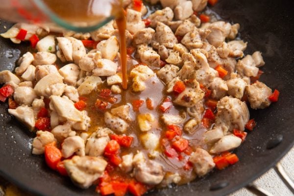 Pouring sauce into the skillet with the chicken and vegetables