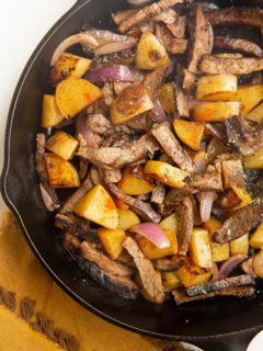 Finished steak and potato skillet in a cast iron skillet with a napkin to the side