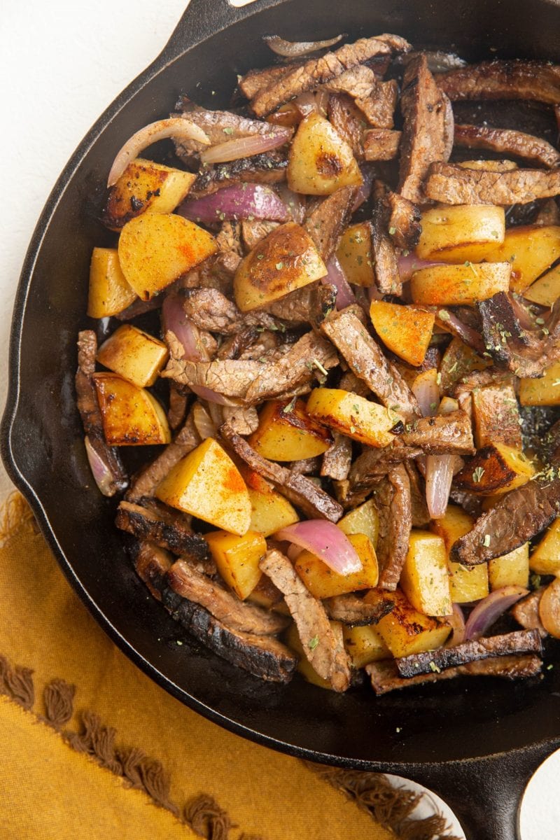 Finished steak and potato skillet in a cast iron skillet with a napkin to the side