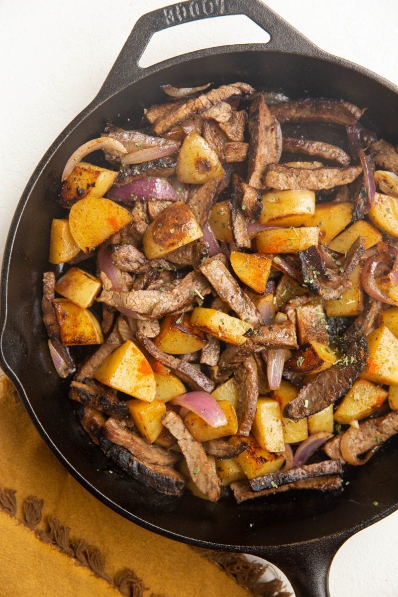 Cast iron skillet with cooked steak, potatoes, and onion.