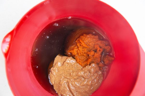 Red mixing bowl with pumpkin puree, almond butter, and pure maple syrup inside.