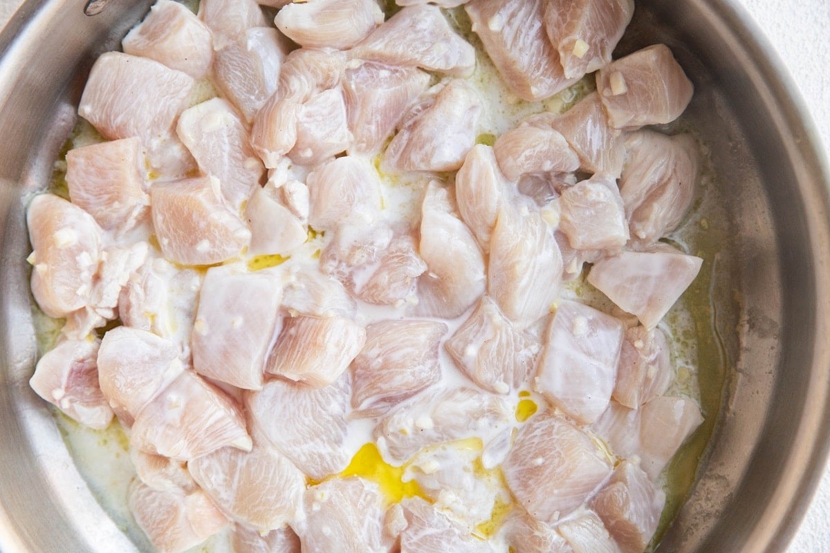 Chicken cooking in a stainless steel skillet.