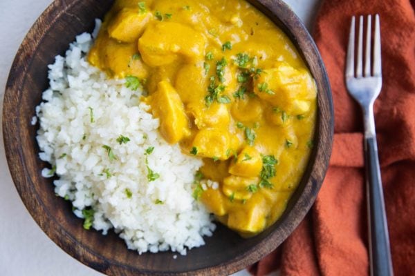 Horizontal image of AIP Chicken TIkka Masala in a wooden bowl with a red napkin next to it.