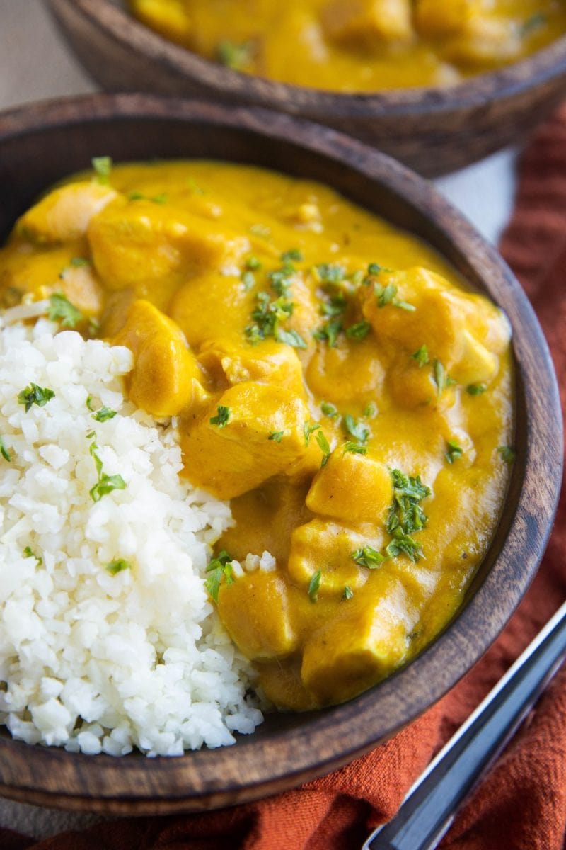 Two wooden bowls of AIP Chicken Tikka Masala with a red napkin to the side.