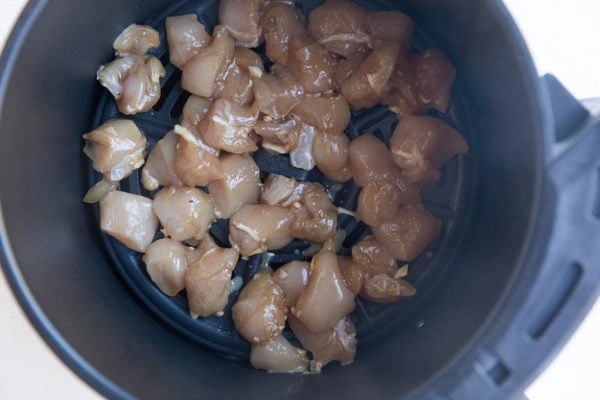 Raw marinated chicken pieces in an air fryer basket.