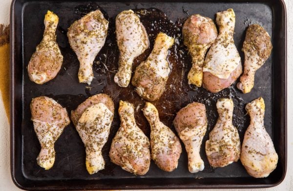 Raw marinated chicken legs on a rimmed baking sheet, ready to go into the oven.