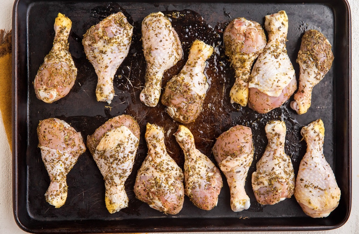 Raw marinated chicken legs on a rimmed baking sheet, ready to go into the oven.