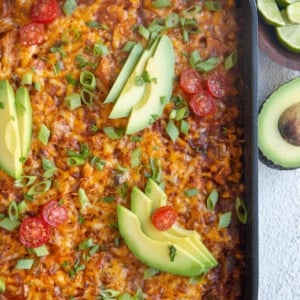 Top down photo of whole enchilada casserole fresh out of the oven with slices of avocado and cherry tomatoes on top.