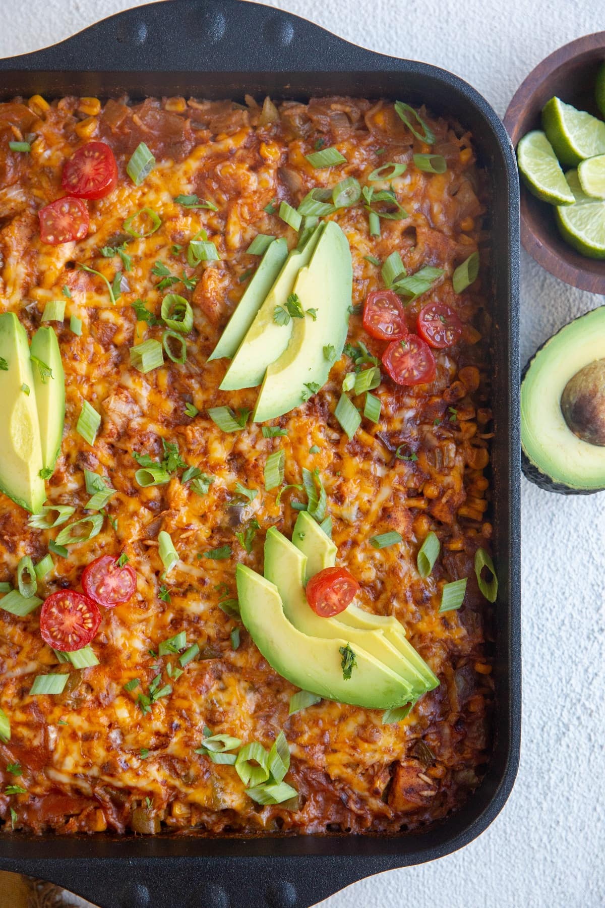 Top down photo of whole enchilada casserole fresh out of the oven with slices of avocado and cherry tomatoes on top.