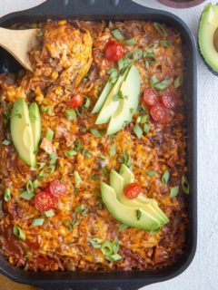 Top down image of cheesy enchilada casserole with a wooden spoon about to serve.