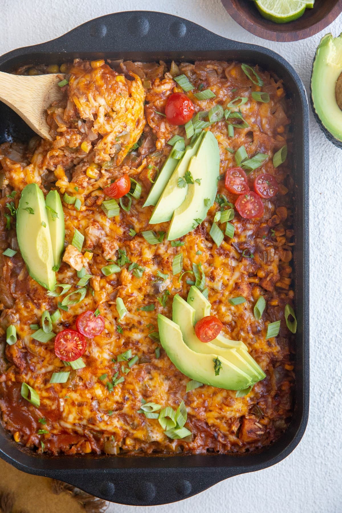 Top down image of cheesy enchilada casserole with a wooden spoon about to serve.