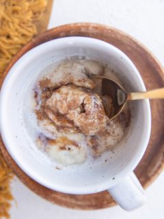 Spoon inside a mug with a single serve cinnamon roll.