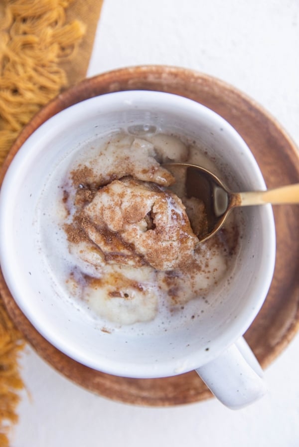 Spoon inside a mug with a single serve cinnamon roll.