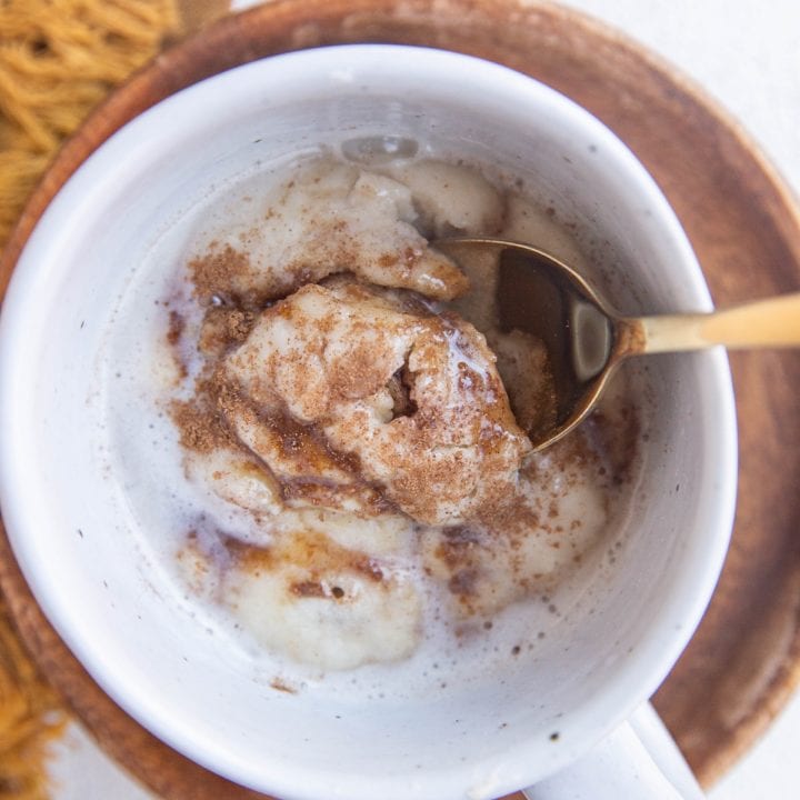 Spoon inside a mug with a single serve cinnamon roll.