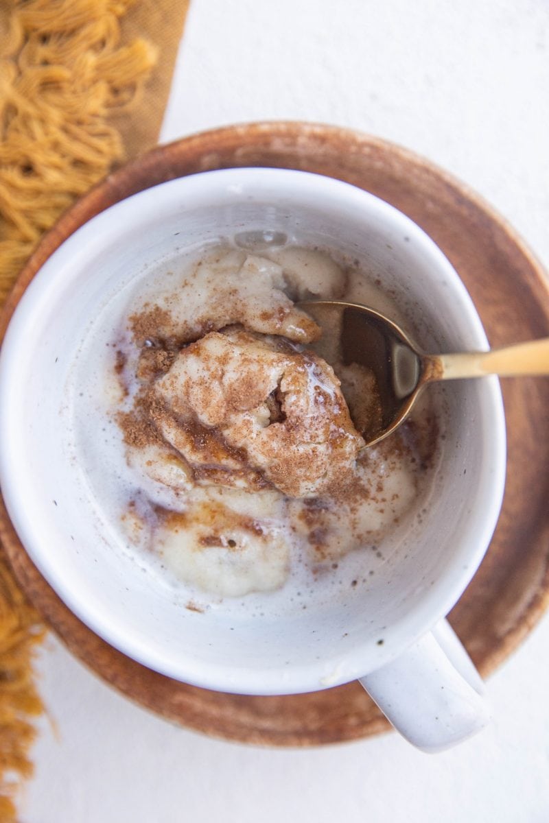 Spoon inside a mug with a single serve cinnamon roll.