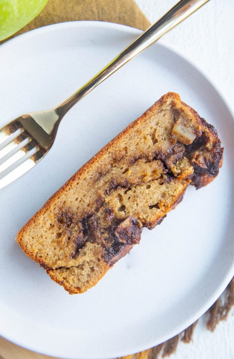 White plate with a slice of apple bread on top, ready to be eaten.