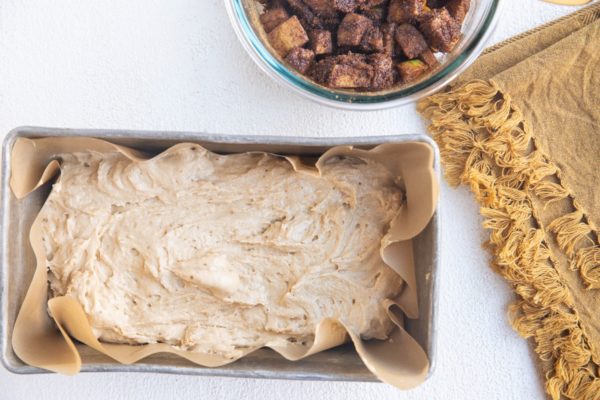 Loaf pan with half of the bread dough spread in it and the apple cinnamon mixture to the side.