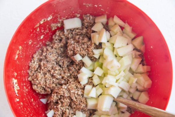 Apple bar dough in a mixing bowl with chunks of apple on top, ready to be mixed in.