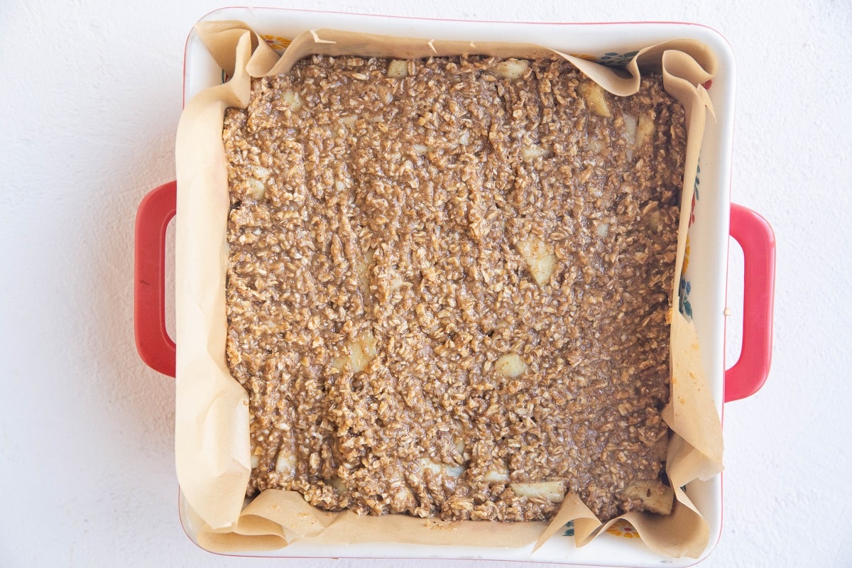 Apple bar dough spread into a baking pan lined with parchment paper.