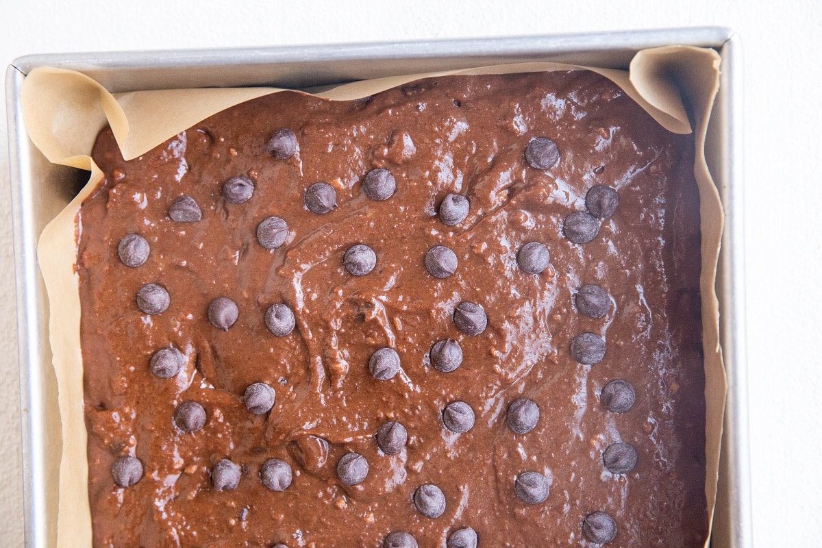 Parchment lined baking pan with brownie batter in it, ready to go into the oven.