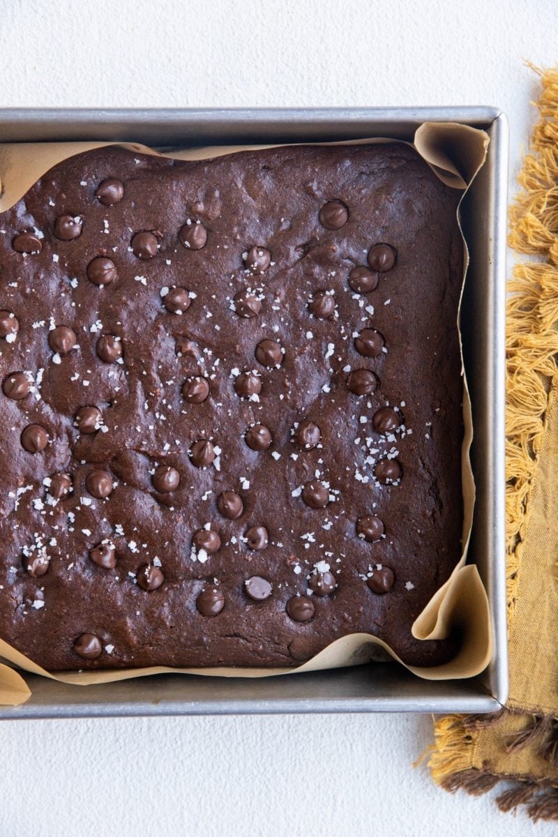 Tray of sweet potato brownies fresh out of the oven with a golden napkin to the side, sprinkled with sea salt.