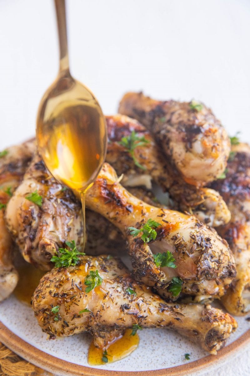 Plate of chicken drumsticks being drizzled with honey.