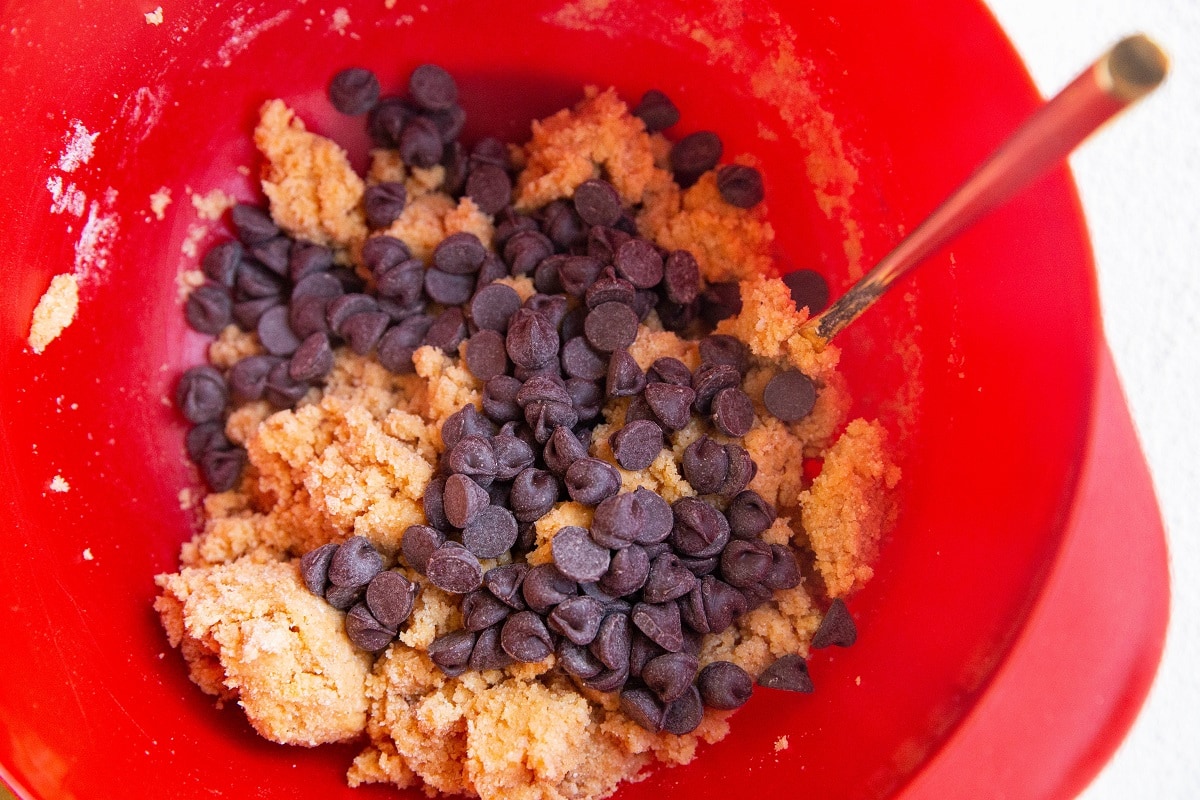 Sugar-free pumpkin cookie dough in a mixing bowl with chocolate chips on top, ready to be mixed in.