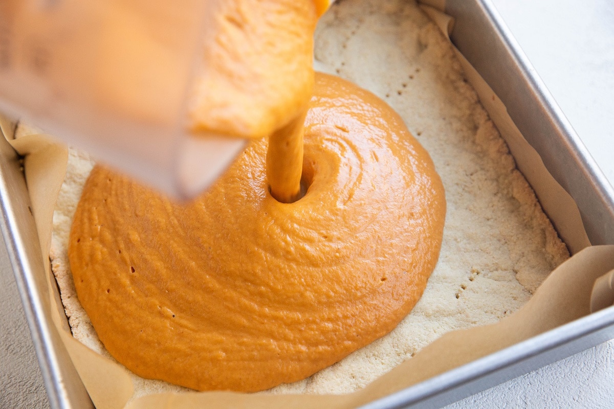 Pouring the pumpkin filling mixture over the crust layer.