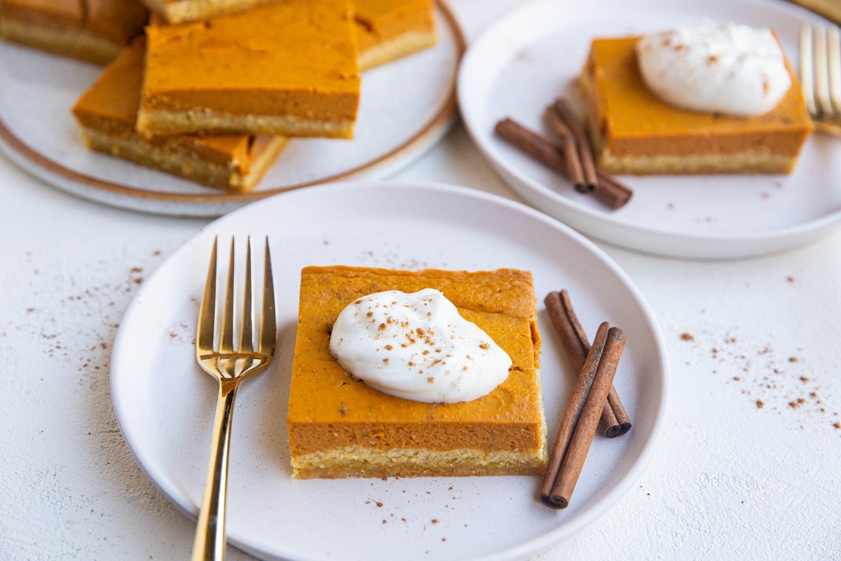 Horizontal image of three plates of sliced pumpkin pie squares.