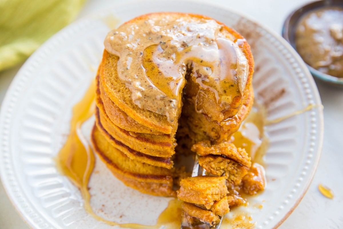 Horizontal photo of a stack of healthy sweet potato pancakes on a plate with a bite taken out.