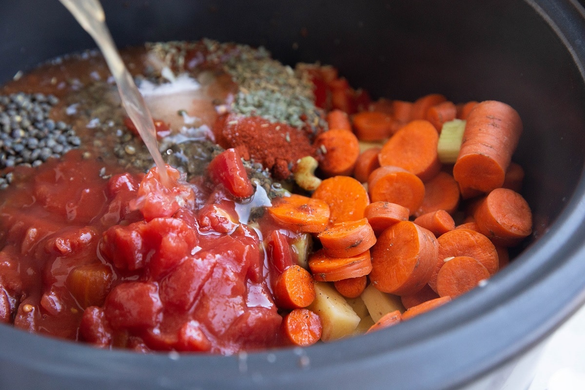 Broth being poured into a slow cooker with soup ingredients.