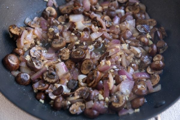 Onion, mushrooms and garlic sautéing in a skillet.