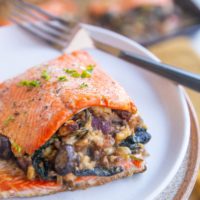 Plate with a stuffed salmon filet on top with a baking sheet of salmon filets in the background.